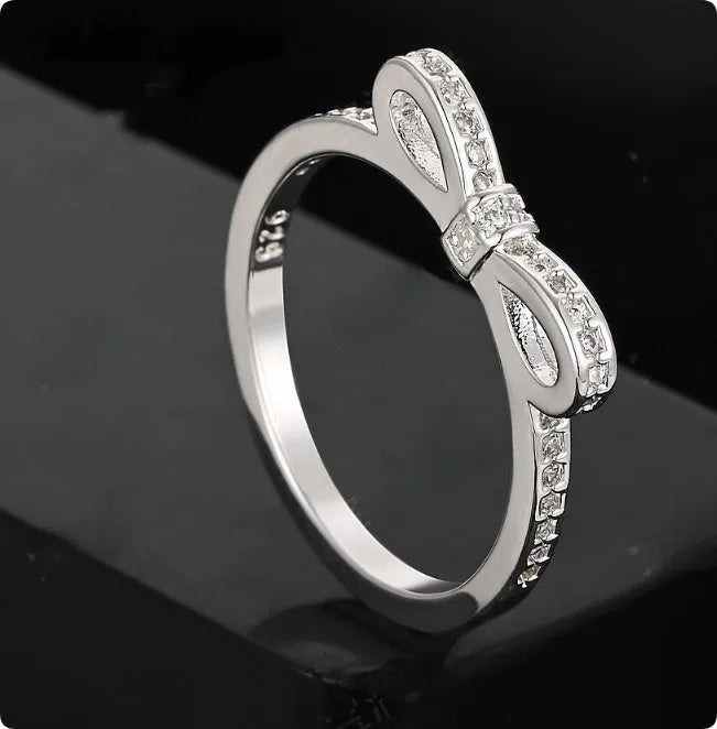 Silver coloured bow-shaped ring with rhinestone and zircon crystal decoration on a model's finger.