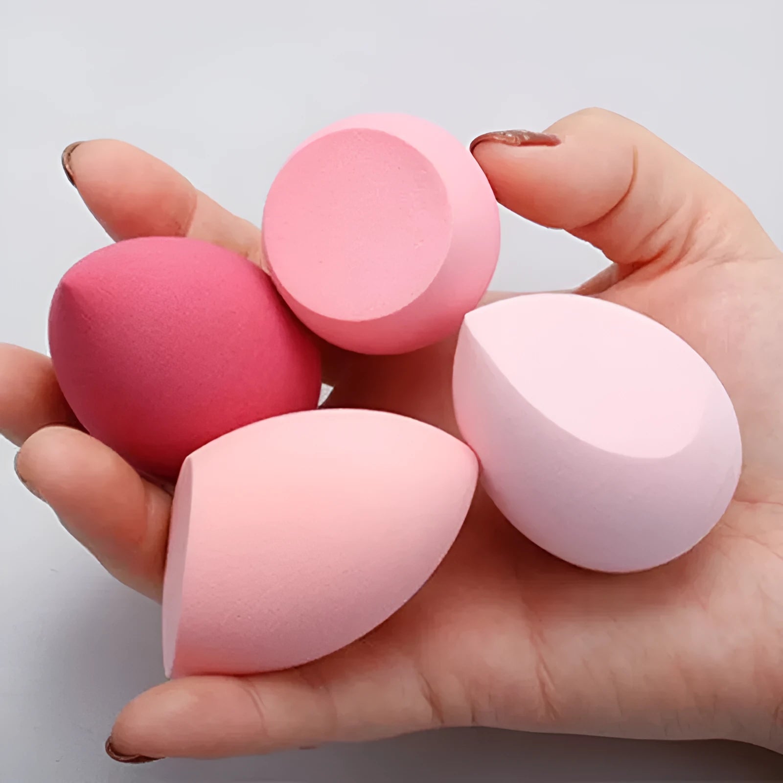 Set of seven differently shaped coloured makeup sponges including pear, heart, and drop shapes on a white background.
