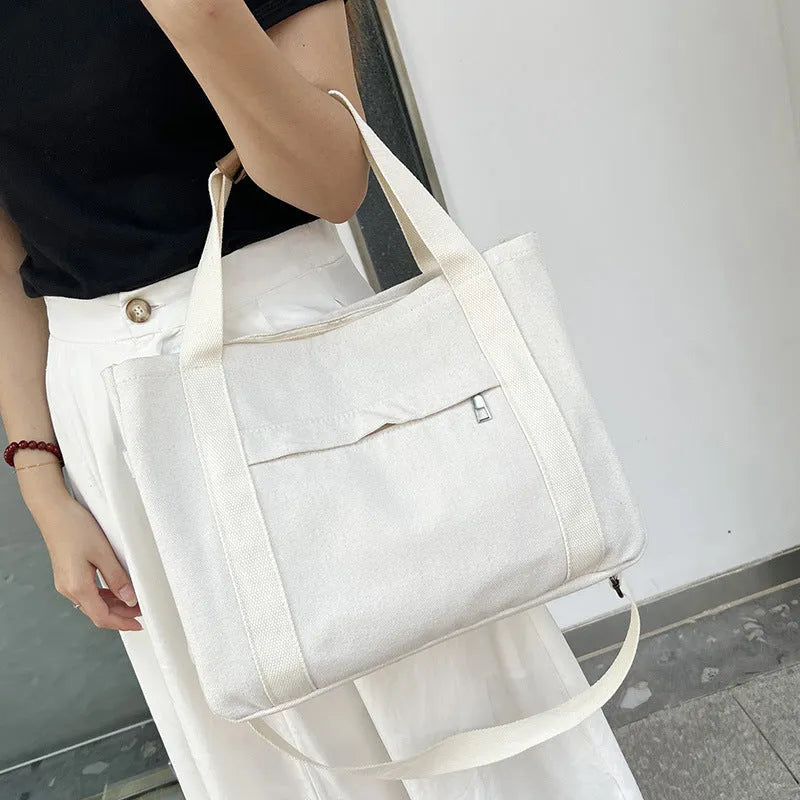 Khaki canvas tote bag with zipper closure showing internal camera pocket and document bag compartments.