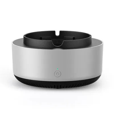 Grey intelligent electronic air purifier ashtray on a desk with cigarette butts in grooved tray.
