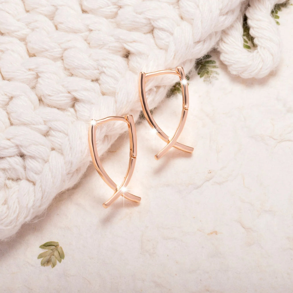 A pair of rose gold coloured cross shaped earrings made from polished copper.