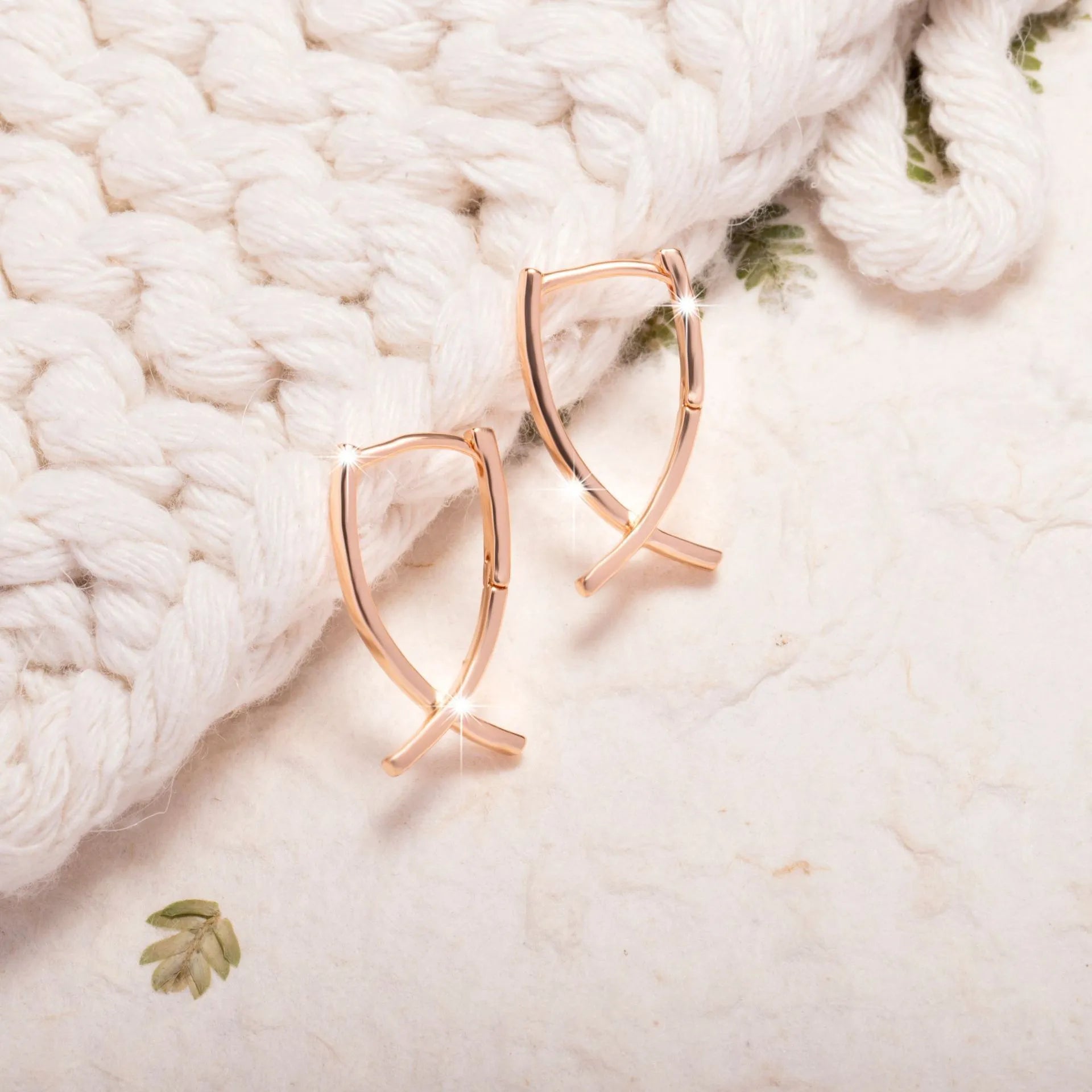 A pair of rose gold coloured cross shaped earrings made from polished copper.
