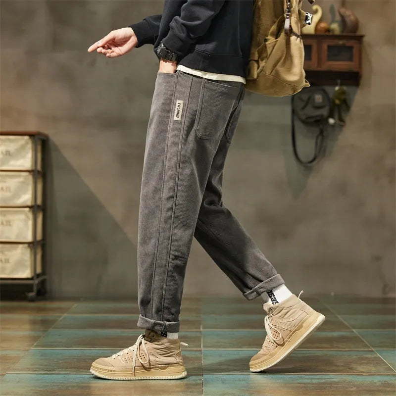 Man wearing tapered straight-leg corduroy trousers in army green, showing mid-rise waist and street style.