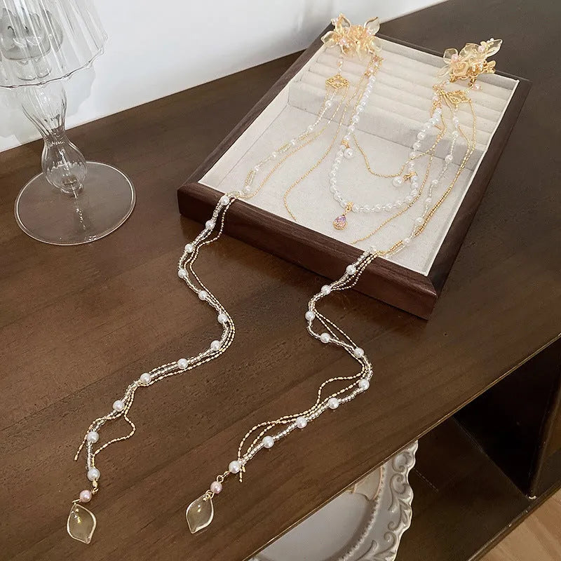 Gold acrylic women's hairpin with white flower, pearl beads, diamond accents, and a long black tassel.