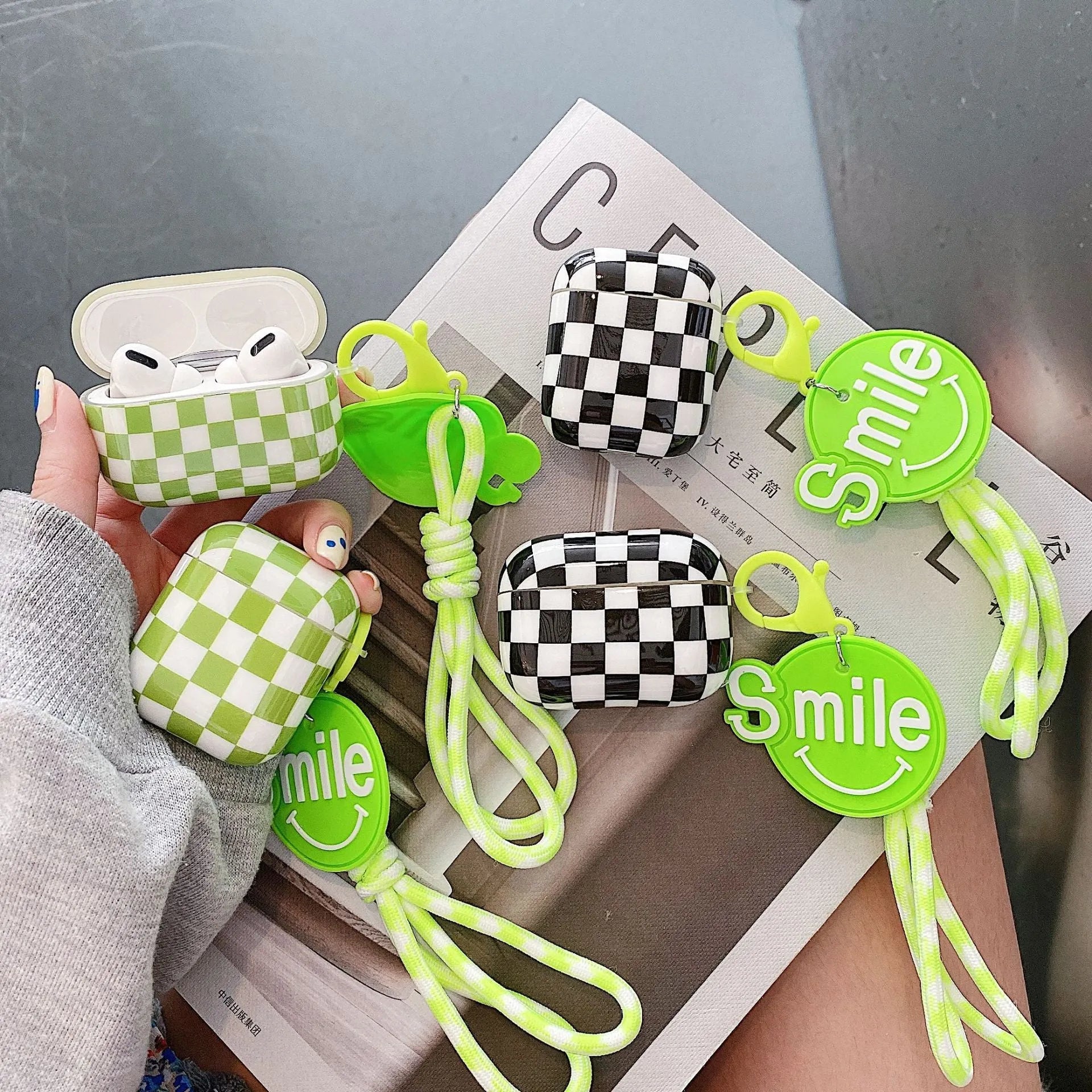 Black and green checkerboard pattern TPU protective case covers for Apple AirPods, one with a smiley face lanyard.