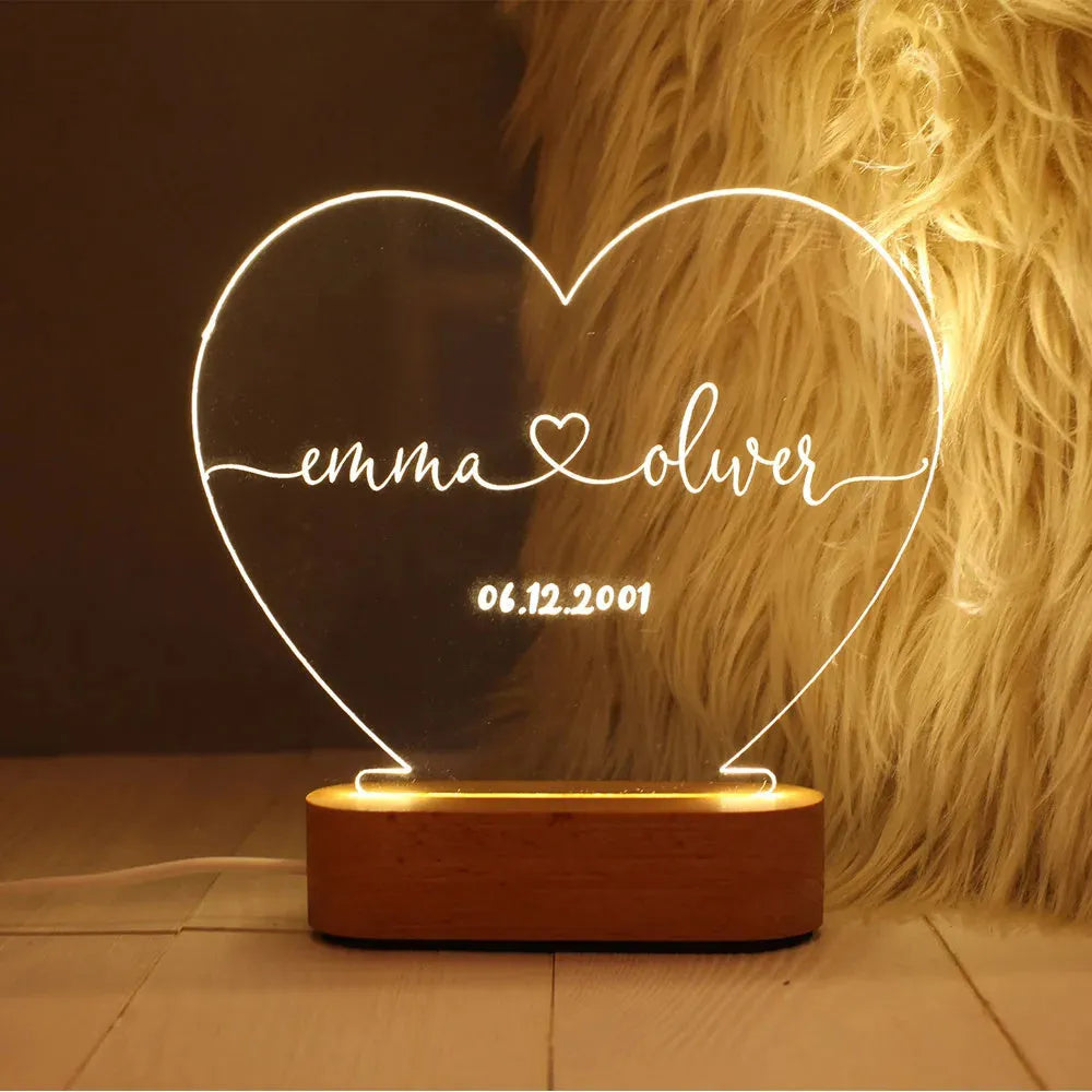 Custom transparent acrylic LED night light engraved with personal names and a date on a bedside table.