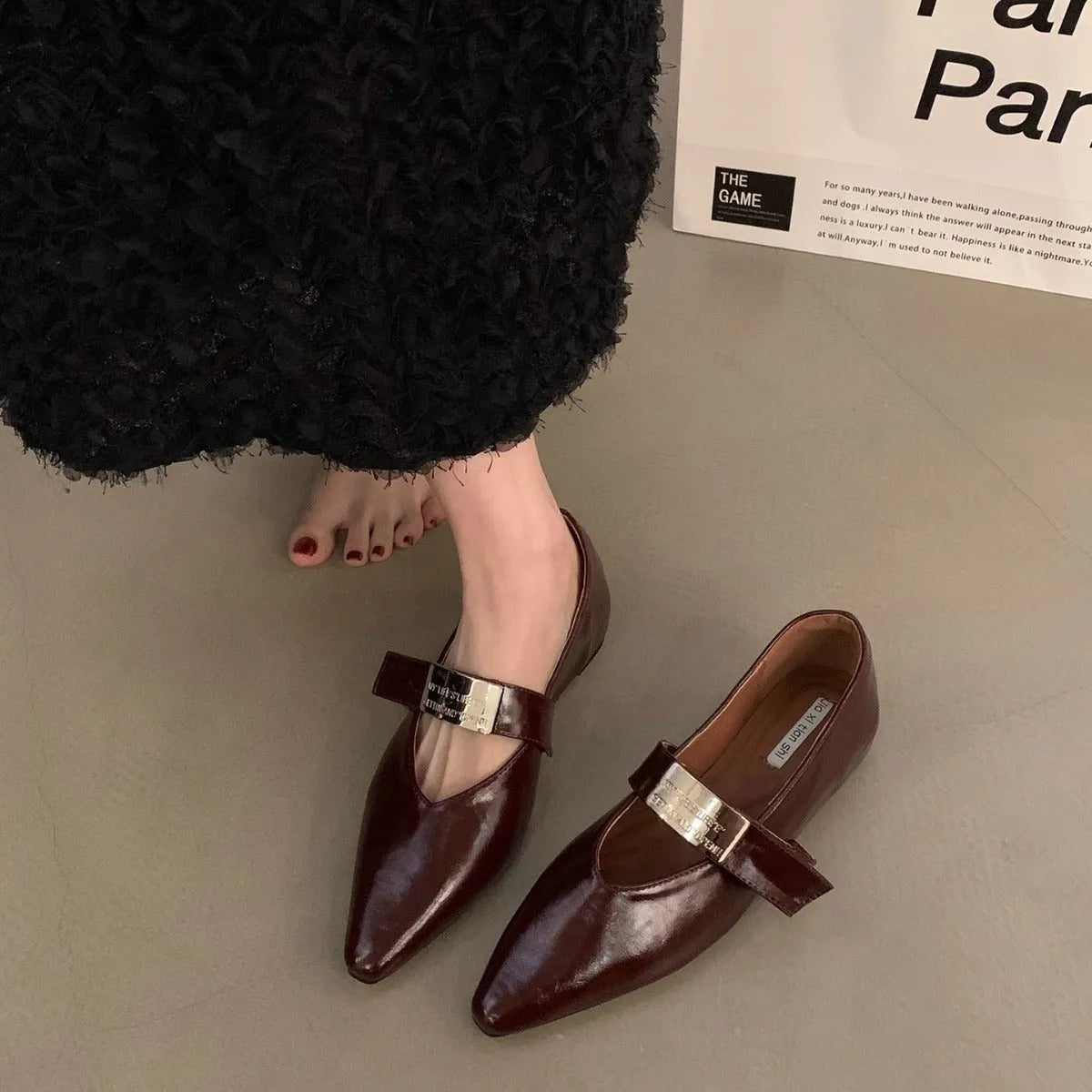 Women's black pointed toe Mary Jane shoes with a silver buckle on a low flat heel.