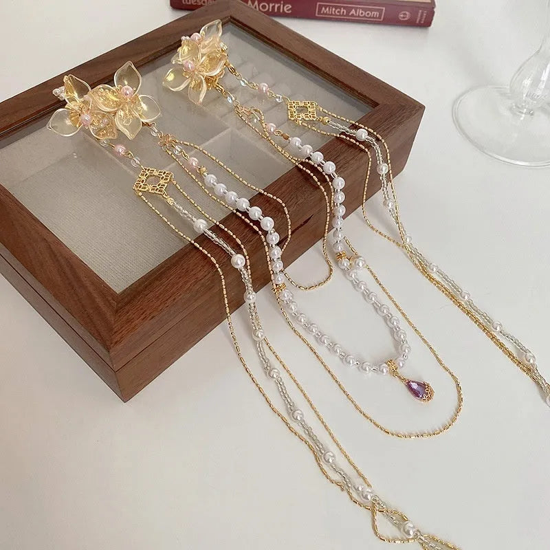 Gold acrylic women's hairpin with white flower, pearl beads, diamond accents, and a long black tassel.