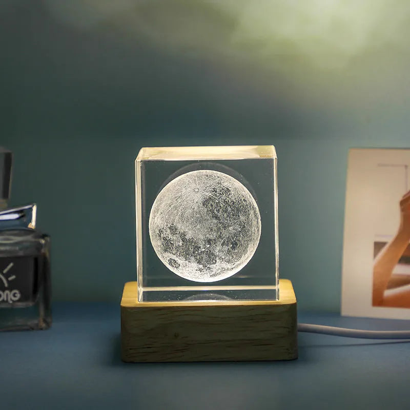 Transparent glass cube night lamp projecting a warm nebula light pattern on a desk.