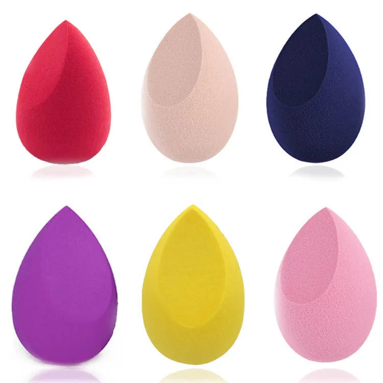 Set of seven differently shaped coloured makeup sponges including pear, heart, and drop shapes on a white background.