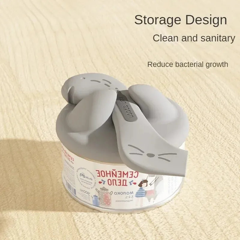 Grey silicone pet food can sealing lid and mixing spoon with integrated can opener on a white background.