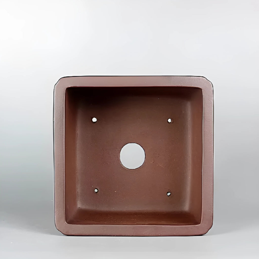 Brown handmade antique flower pot made from purple clay on a windowsill.