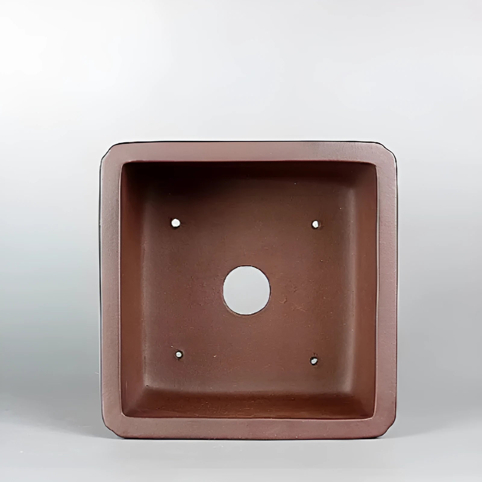 Brown handmade antique flower pot made from purple clay on a windowsill.