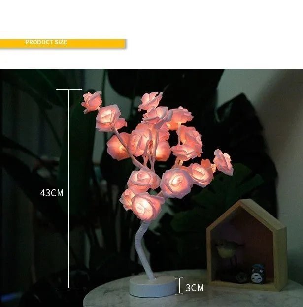 White and red rose shaped LED table lamp with bonsai tree base on a wooden table.