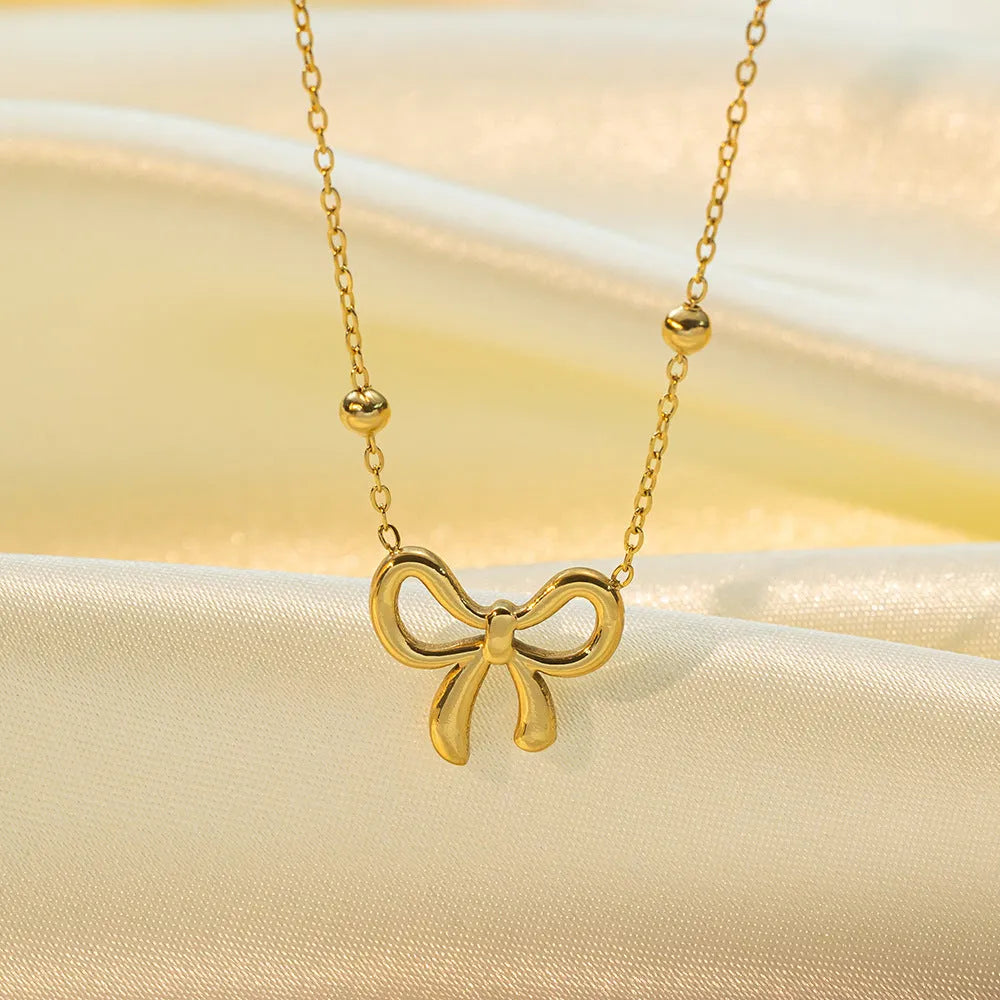 Gold coloured bow pendant necklace on a cross chain, showing adjustable length.