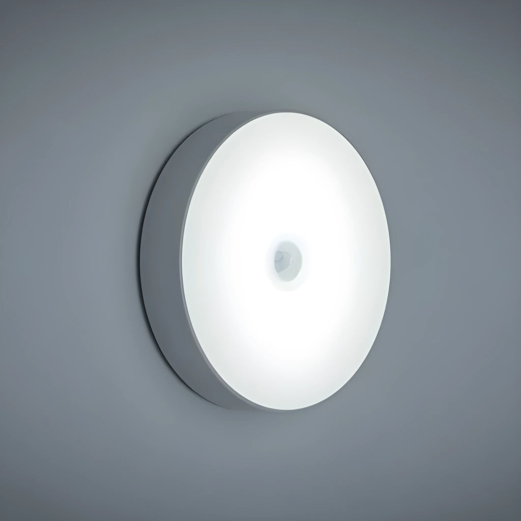 Small circular beige and white LED body sensor night light with USB charging cable on a surface.