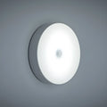 Small circular beige and white LED body sensor night light with USB charging cable on a surface.