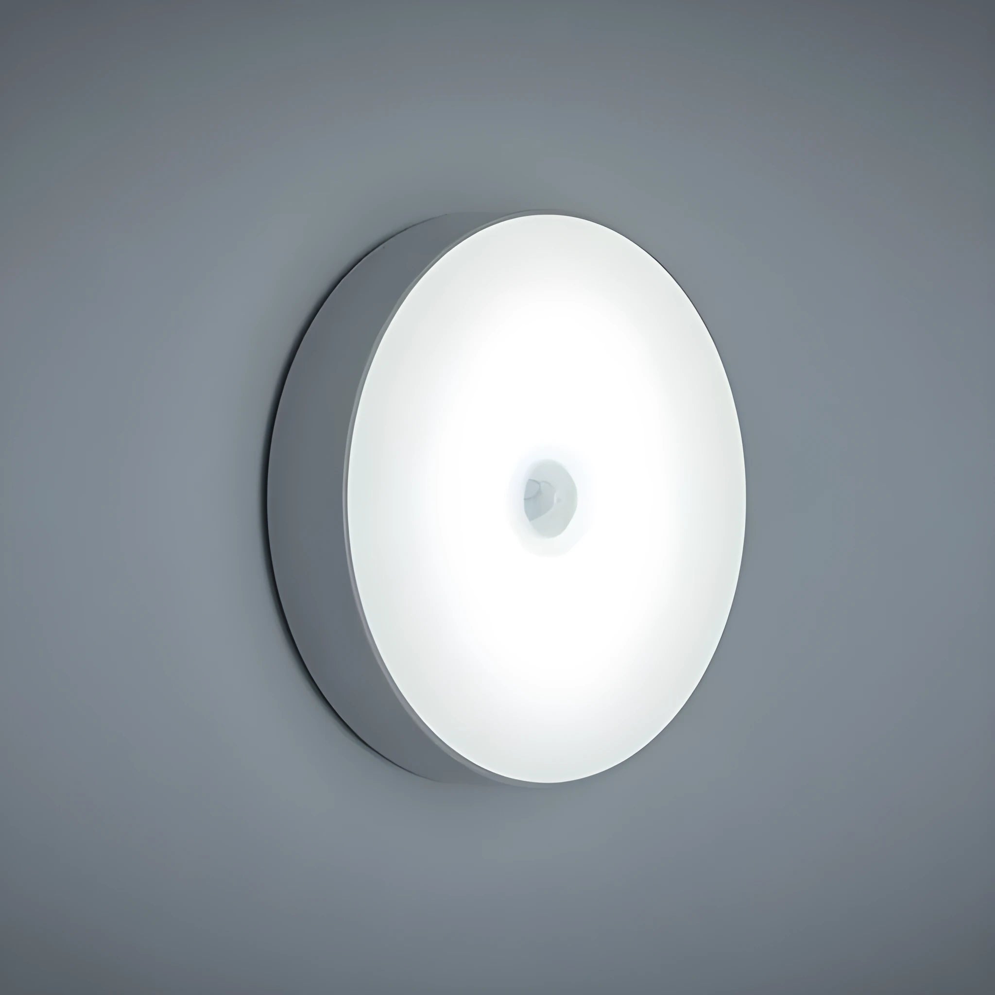 Small circular beige and white LED body sensor night light with USB charging cable on a surface.