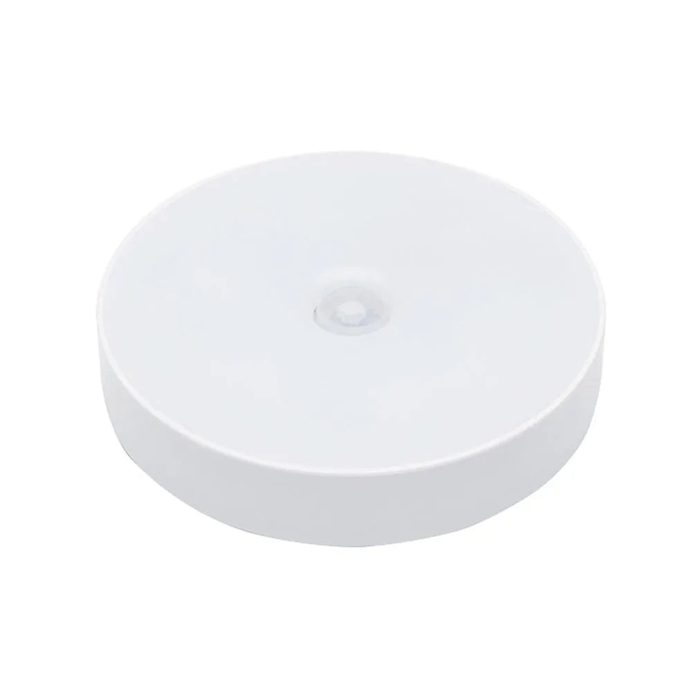 Small circular beige and white LED body sensor night light with USB charging cable on a surface.