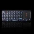 Black wireless mini keyboard with touch screen and laser pointer on a desk next to a laptop