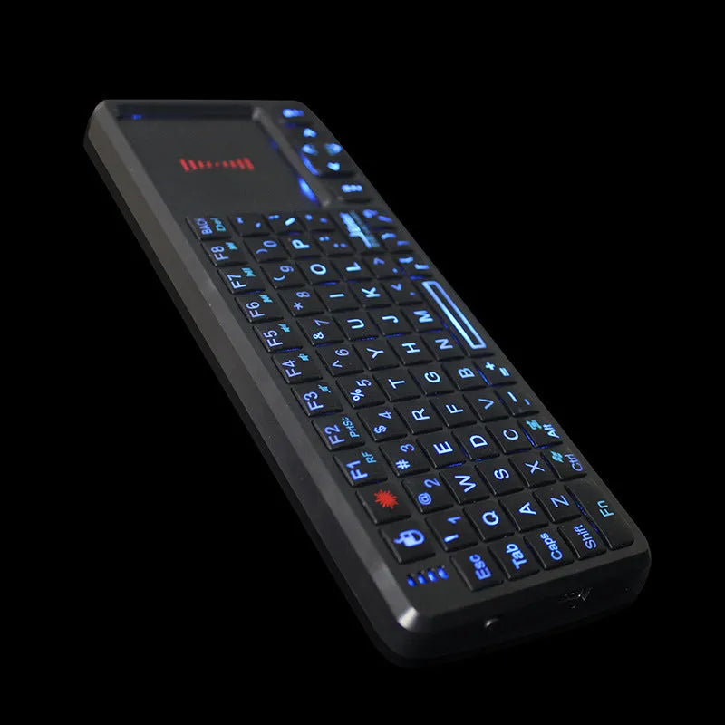 Black wireless mini keyboard with touch screen and laser pointer on a desk next to a laptop