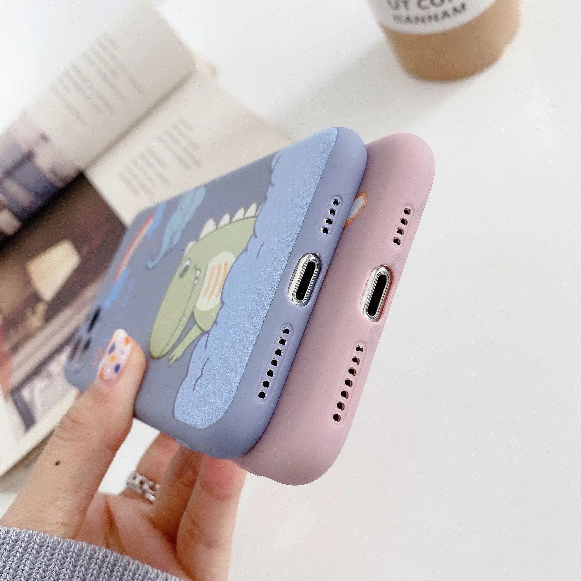 Blue frosted soft shell iPhone case with cartoon dinosaur print next to pink case with cat girl print.