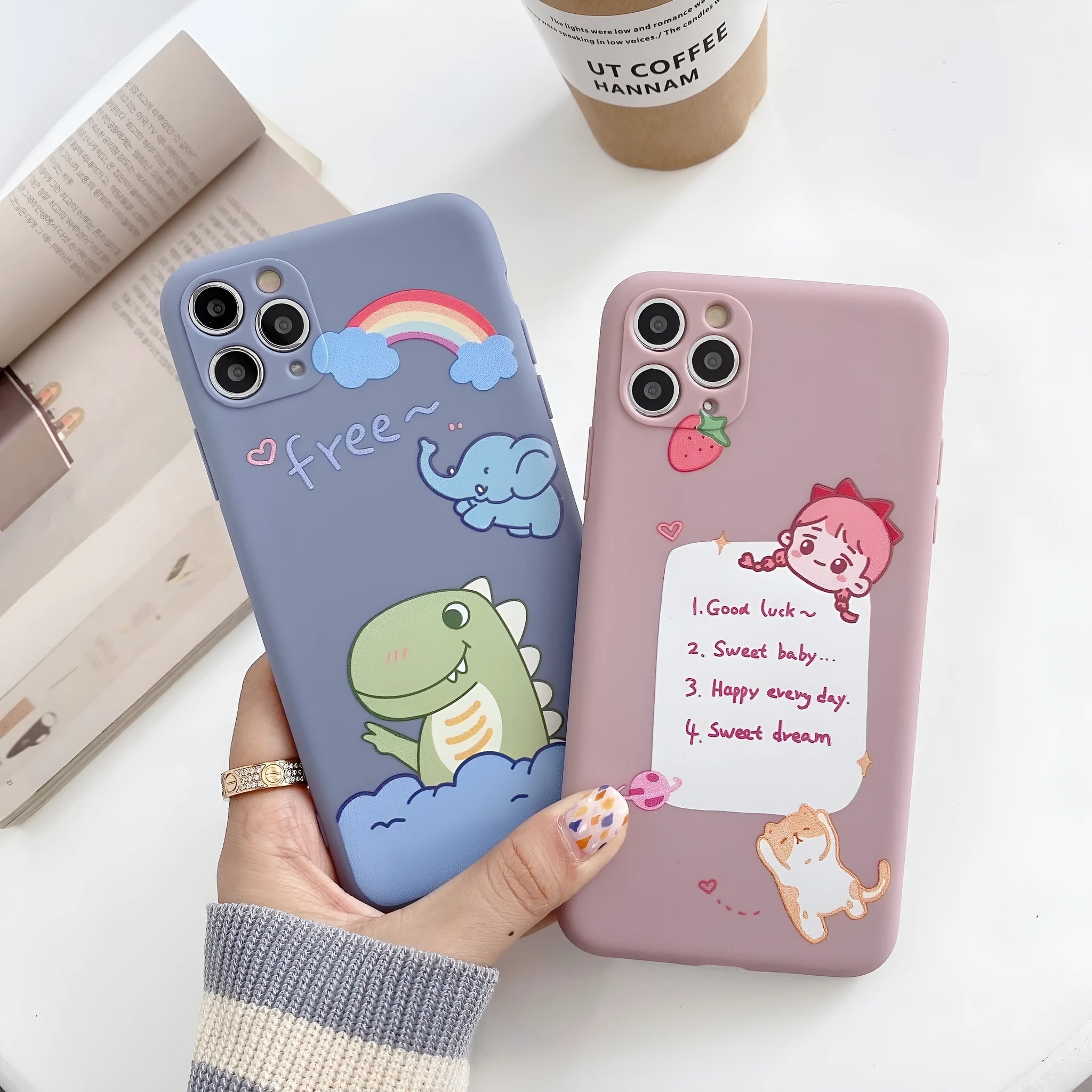 Blue frosted soft shell iPhone case with cartoon dinosaur print next to pink case with cat girl print.