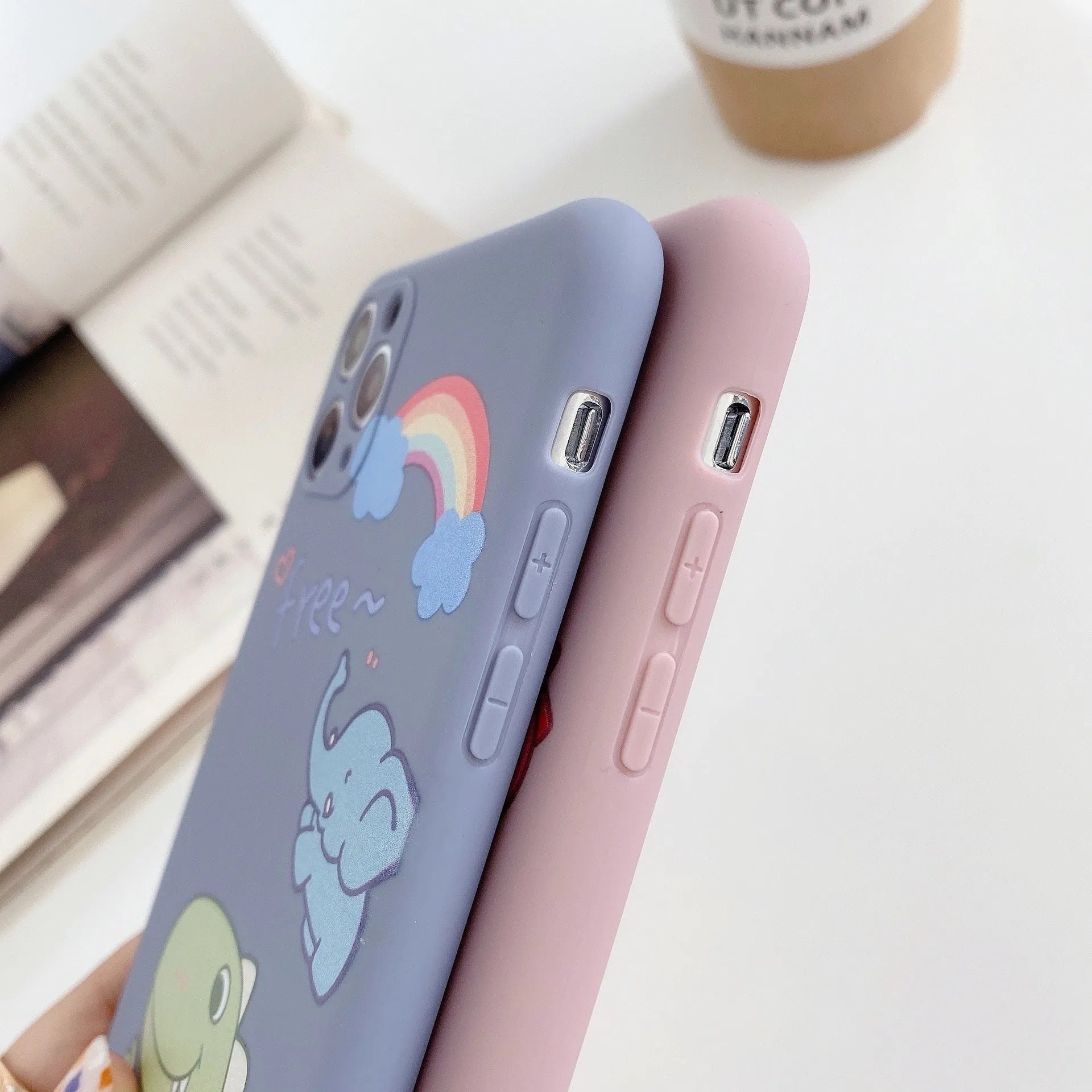 Blue frosted soft shell iPhone case with cartoon dinosaur print next to pink case with cat girl print.