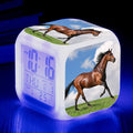 Square cartoon-style LED alarm clock showing colour-changing display on a bedside table.