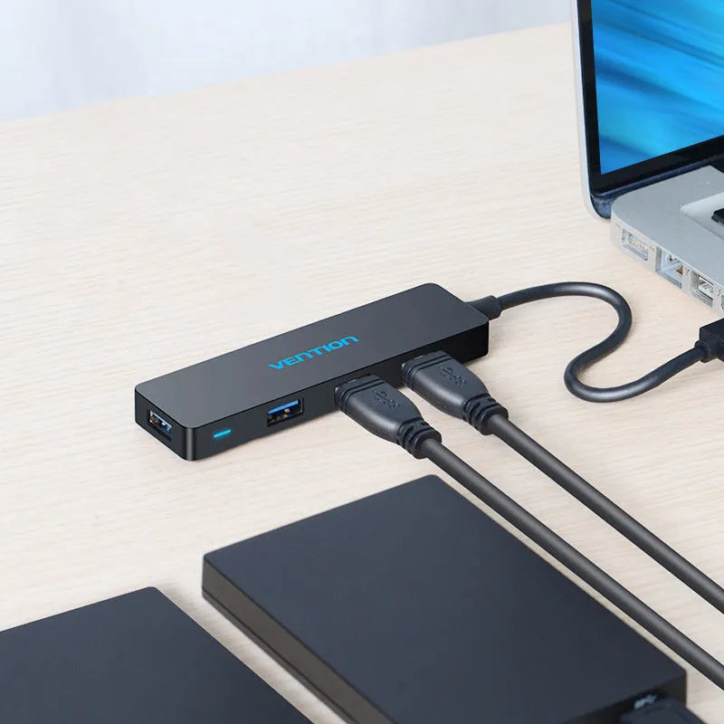 Black four-port USB 3.0 hub with a short 15cm cable on a desk.