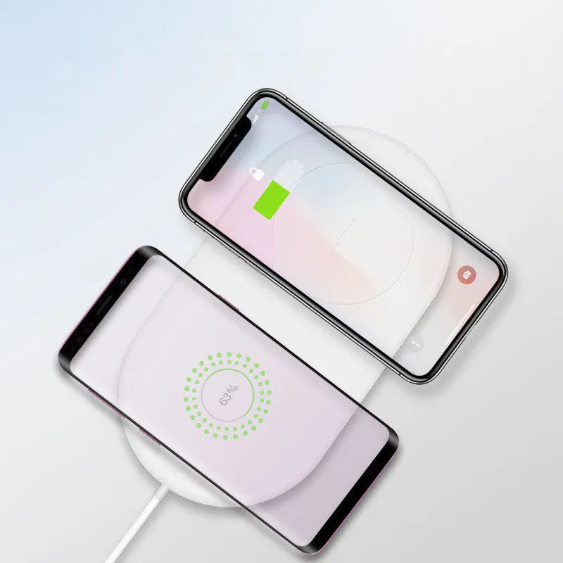 White dual wireless charger charging two mobile phones simultaneously on a simple charging pad