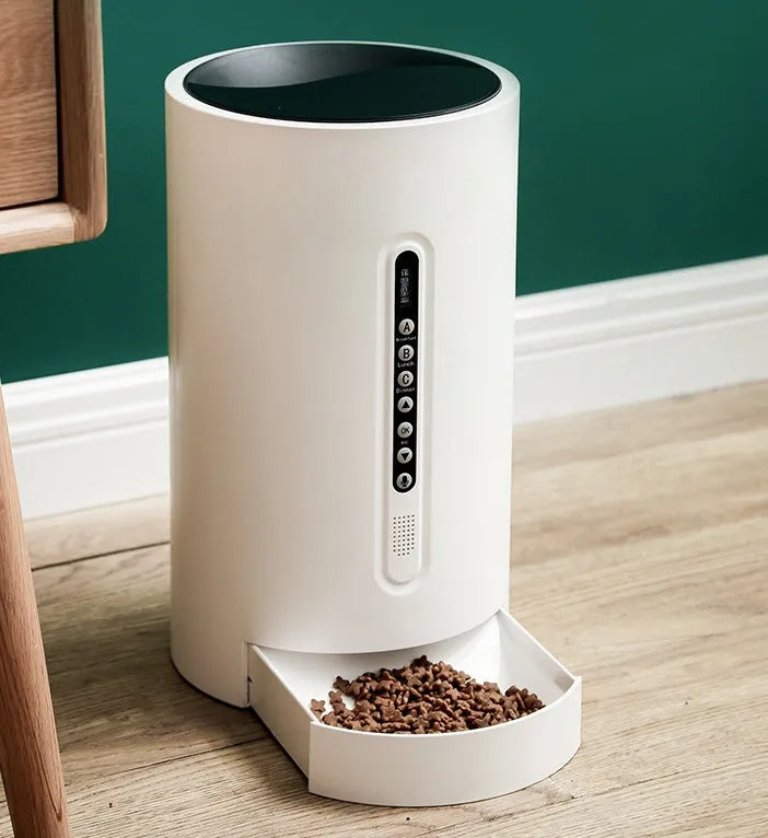 White automatic smart pet feeder with digital timer and large food hopper on a kitchen counter.