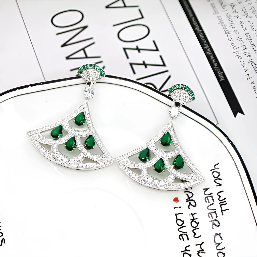 Silver fan-shaped earring with gold-plated inlay of artificial gems, on a plain background