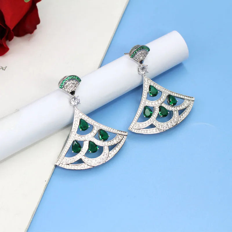 Silver fan-shaped earring with gold-plated inlay of artificial gems, on a plain background
