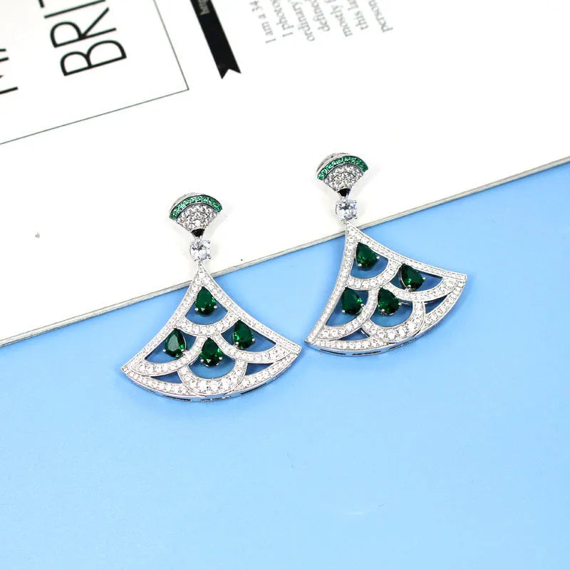 Silver fan-shaped earring with gold-plated inlay of artificial gems, on a plain background