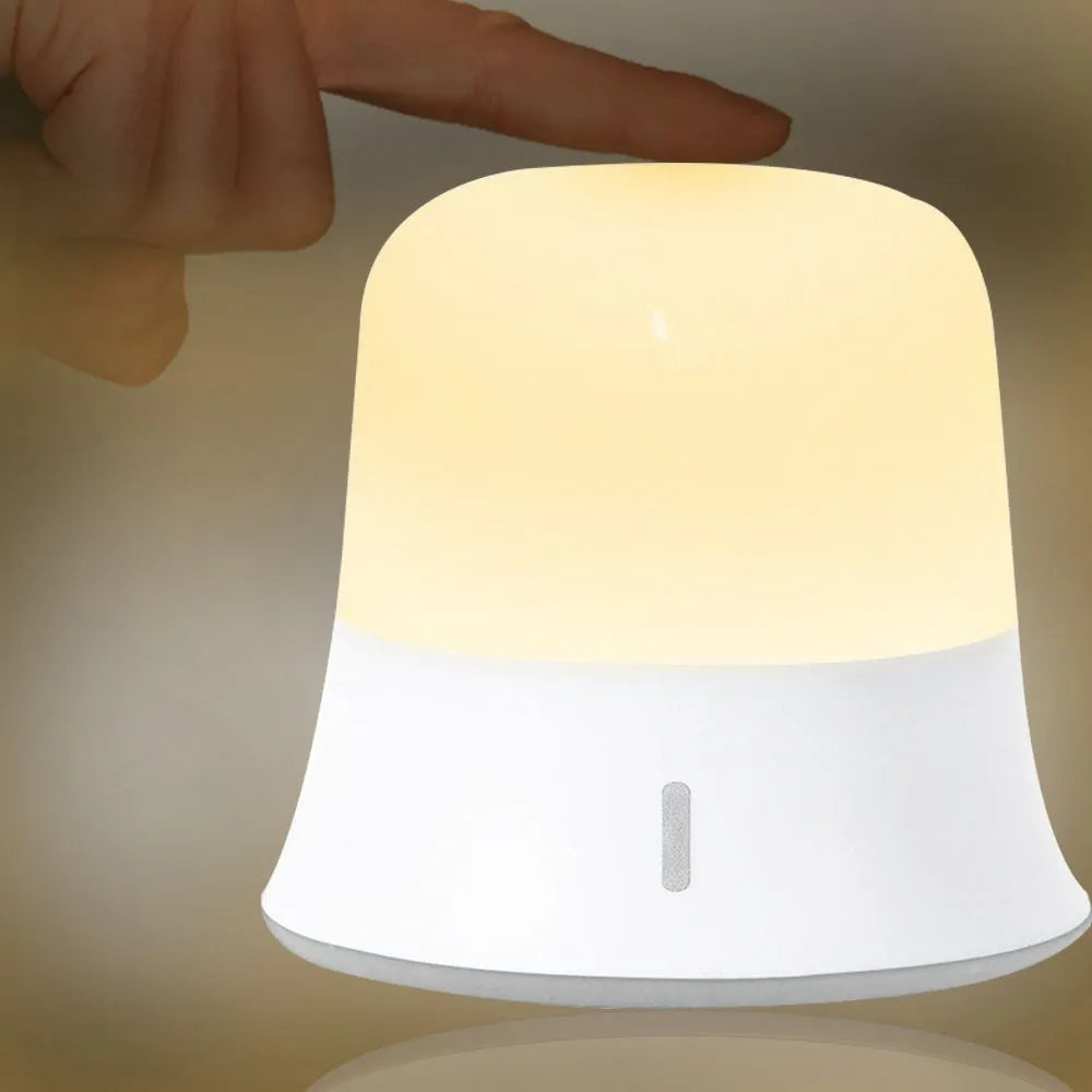 White rechargeable touch-control bedside night light with motion sensor on a table.