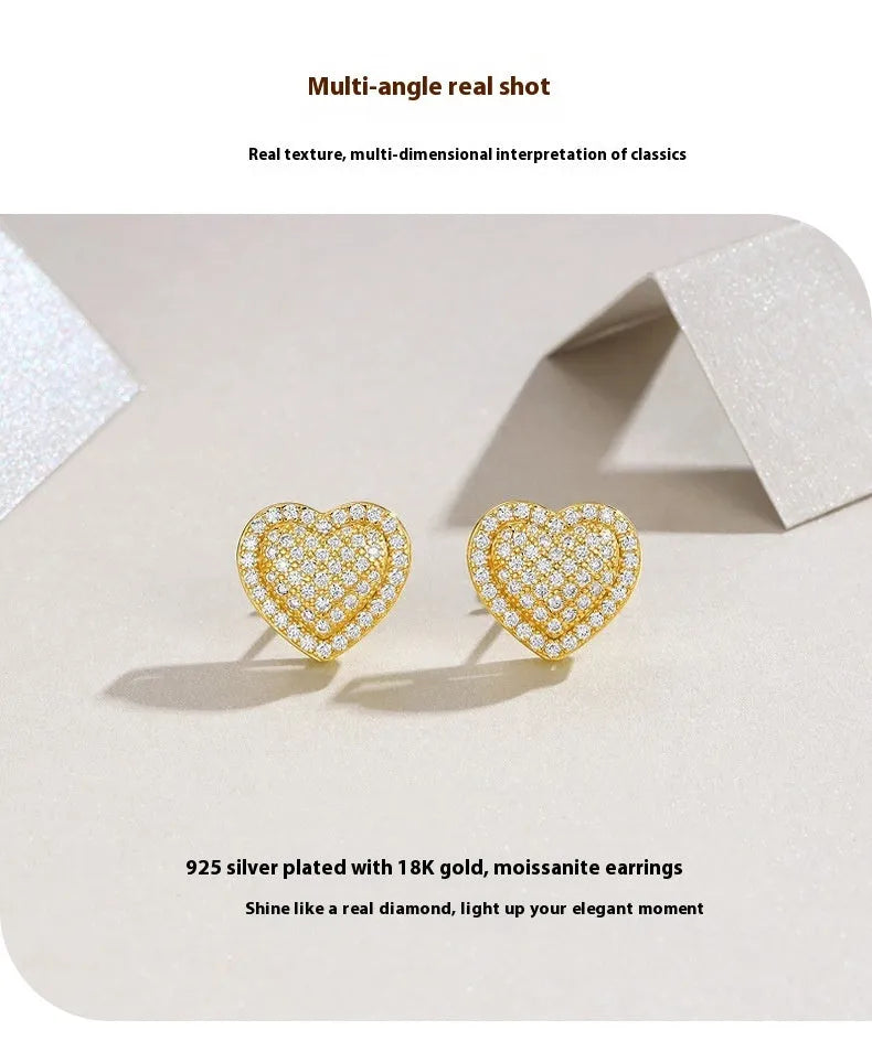 A pair of golden heart-shaped stud earrings with moissanite stones on a grey background.