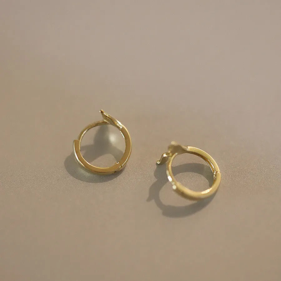 A pair of smooth sterling silver fishtail hoop earrings with a gold plated finish.