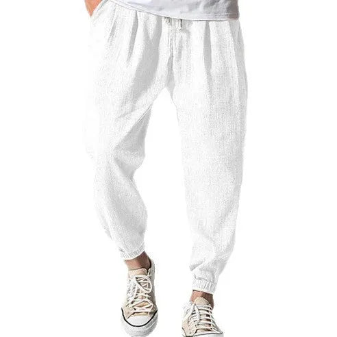 Men's loose fit cotton trousers with elasticated ankle bands in light green, shown in a casual summer setting.