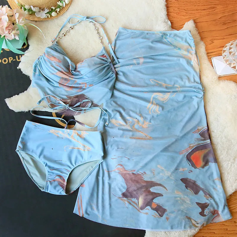 Blue printed women's three-piece bikini set with triangle top, high-waisted briefs, and skirt on hanger.