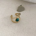 Geometric titanium steel open ring with a central natural green stone on a hand.
