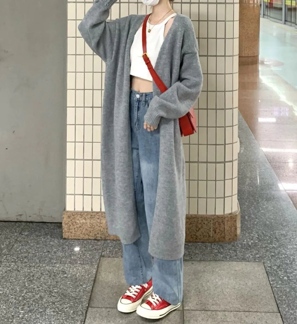 Woman wearing a loose, thick dark gray knitted cardigan with a 3D pattern and long sleeves.