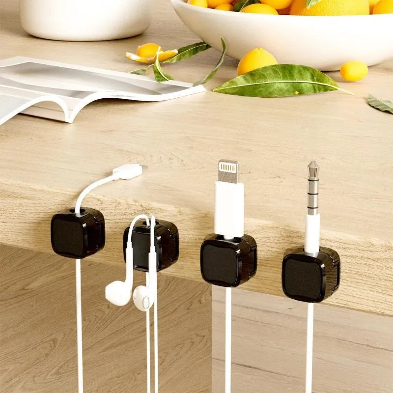 White and black magnetic adhesive cable clips holding a USB cable against a wooden desk.