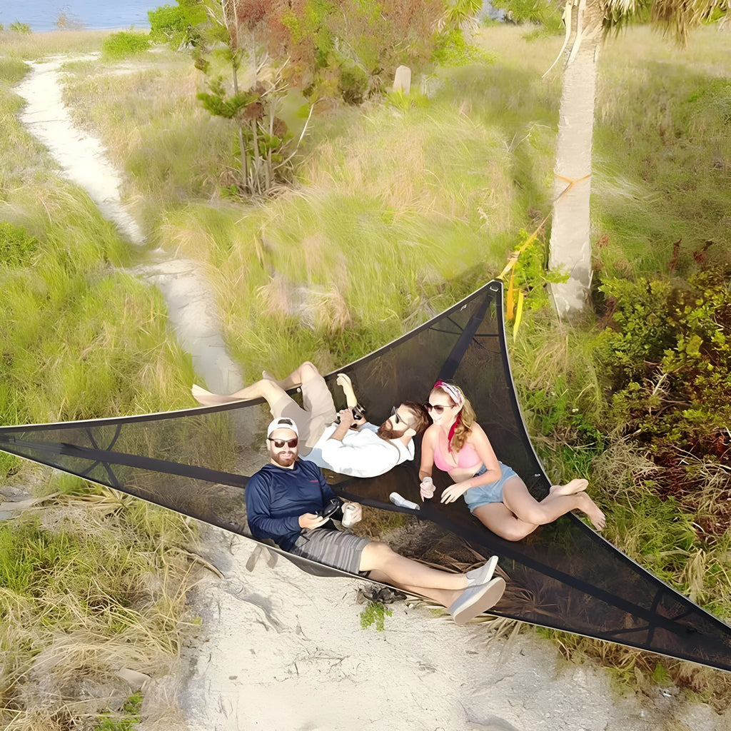 Black polyester portable multi-person triangle hammock lying on grass with trees in background