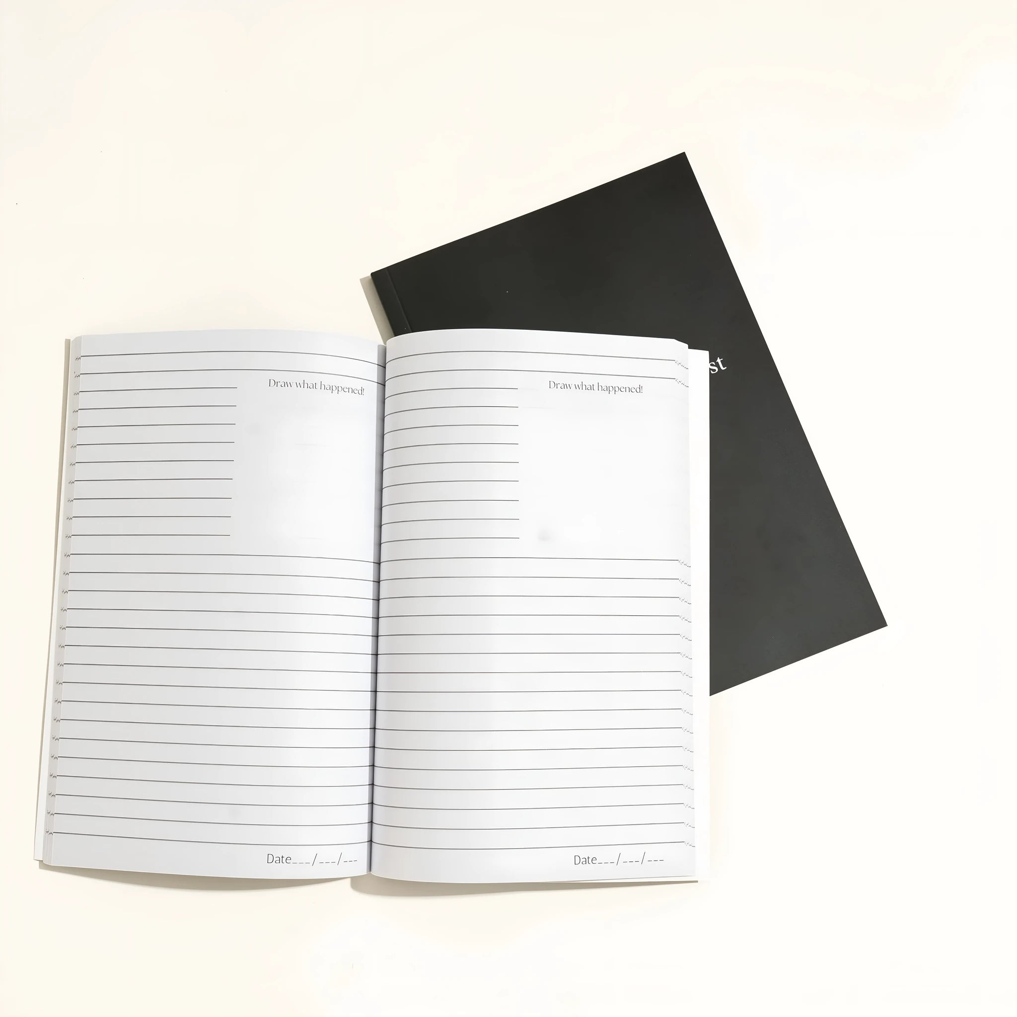 Black soft-touch dream journal notebook lying open on a table, showing ruled pages.