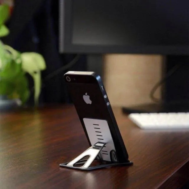 Black card phone holder bracket measuring 8.5cm by 5cm on desktop