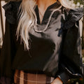 Black women's V-neck blouse with contrast stitching on the neckline and long sleeves with a ruffle detail.