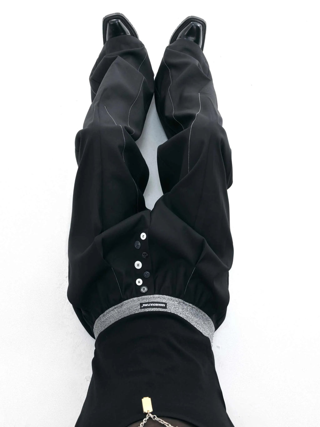 Men's black drooping straight-leg suit trousers with high waist and button detail.