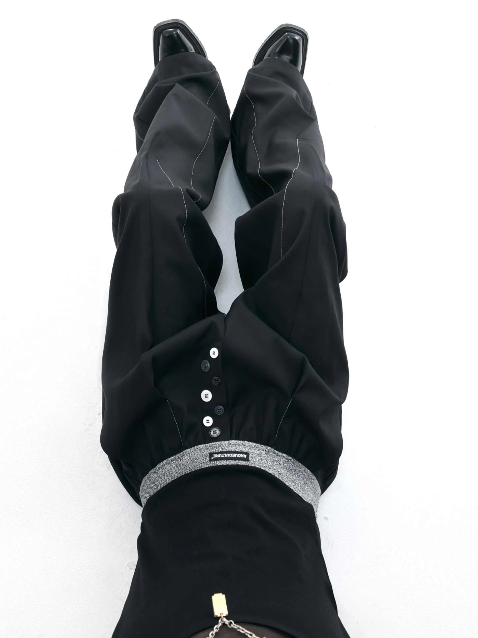 Men's black drooping straight-leg suit trousers with high waist and button detail.