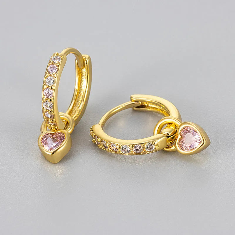 Close-up of women's fashion clip-on earrings with a heart-shaped pink cubic zirconia stone in a gold-coloured copper setting.